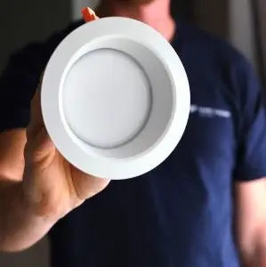 An electrician holding a LED pot light upgrade that is used in residential homes.